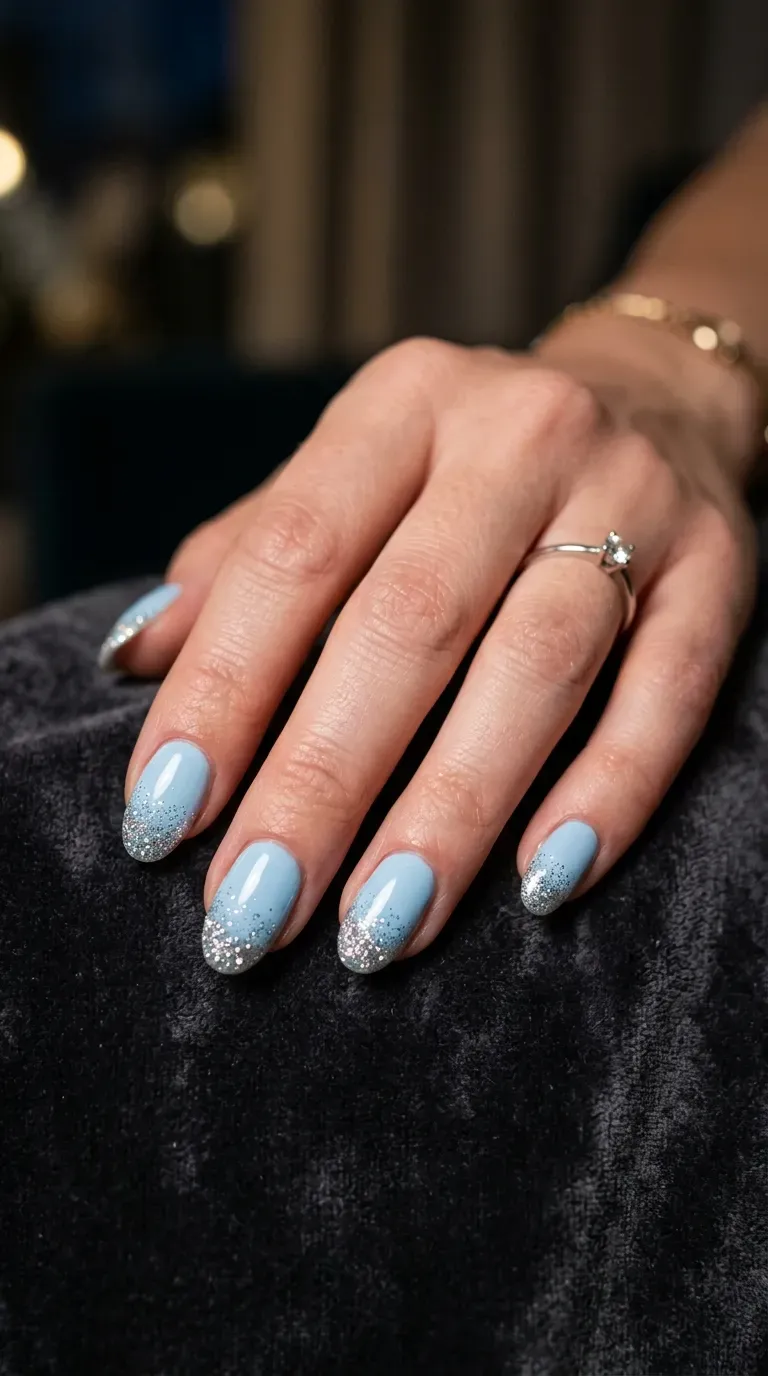 Close-up of manicured hand with light blue nails featuring silver glitter tips