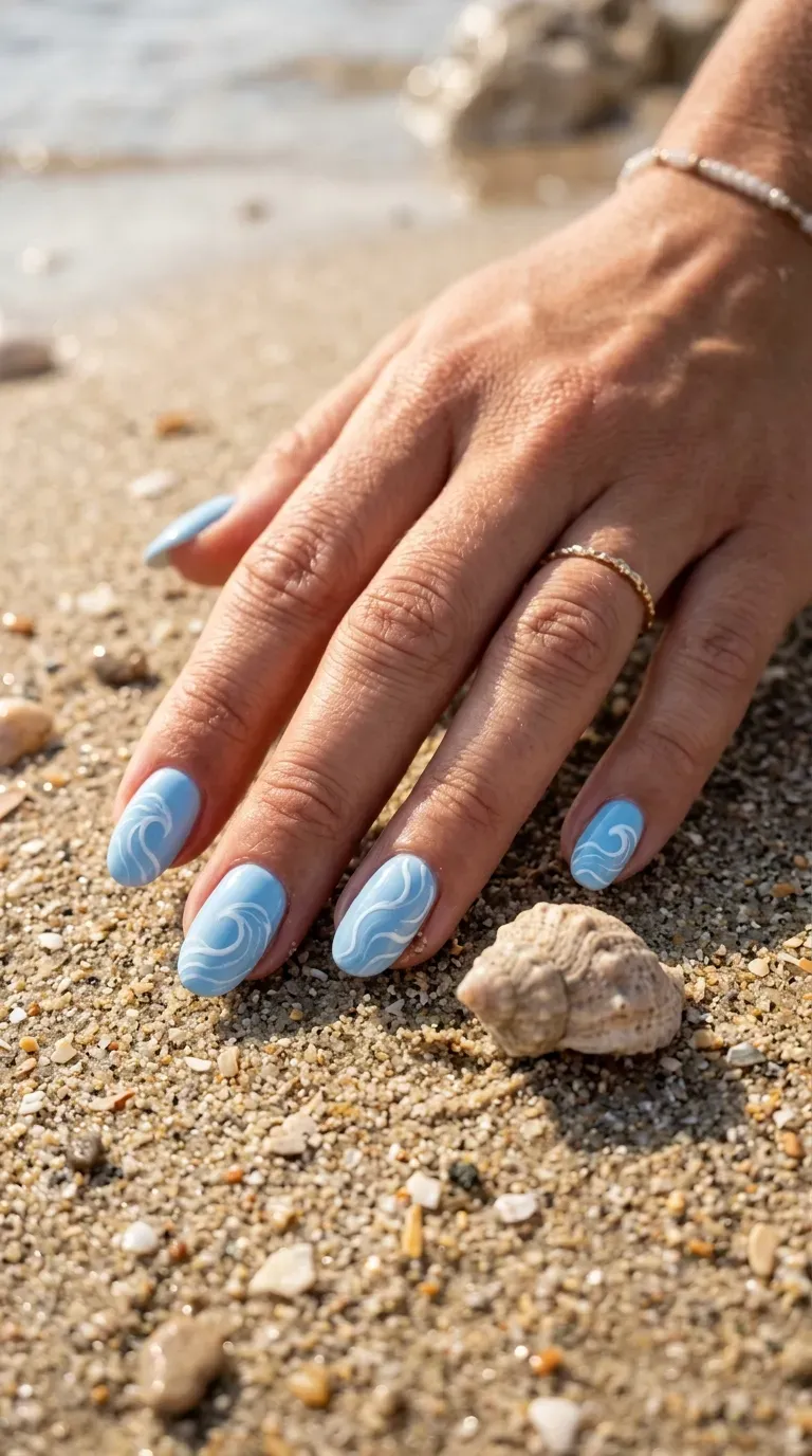 Close-up of manicured hand with light blue nails featuring hand-painted wave patterns