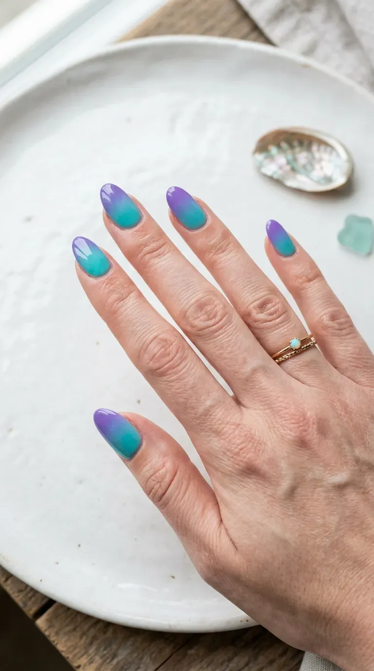Close-up of manicured hand with teal-to-purple ombre mermaid nail design