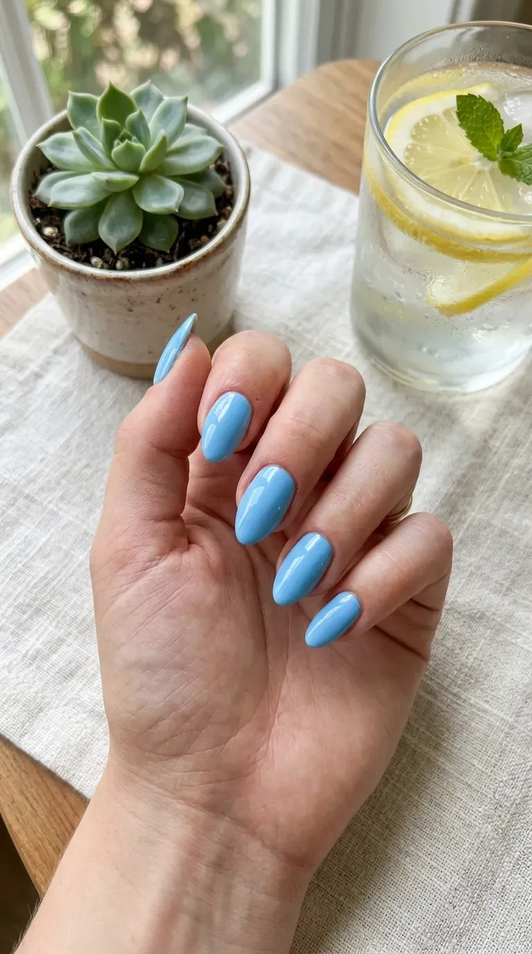 Close-up of manicured hand with sky blue glossy nail polish on medium almond nails